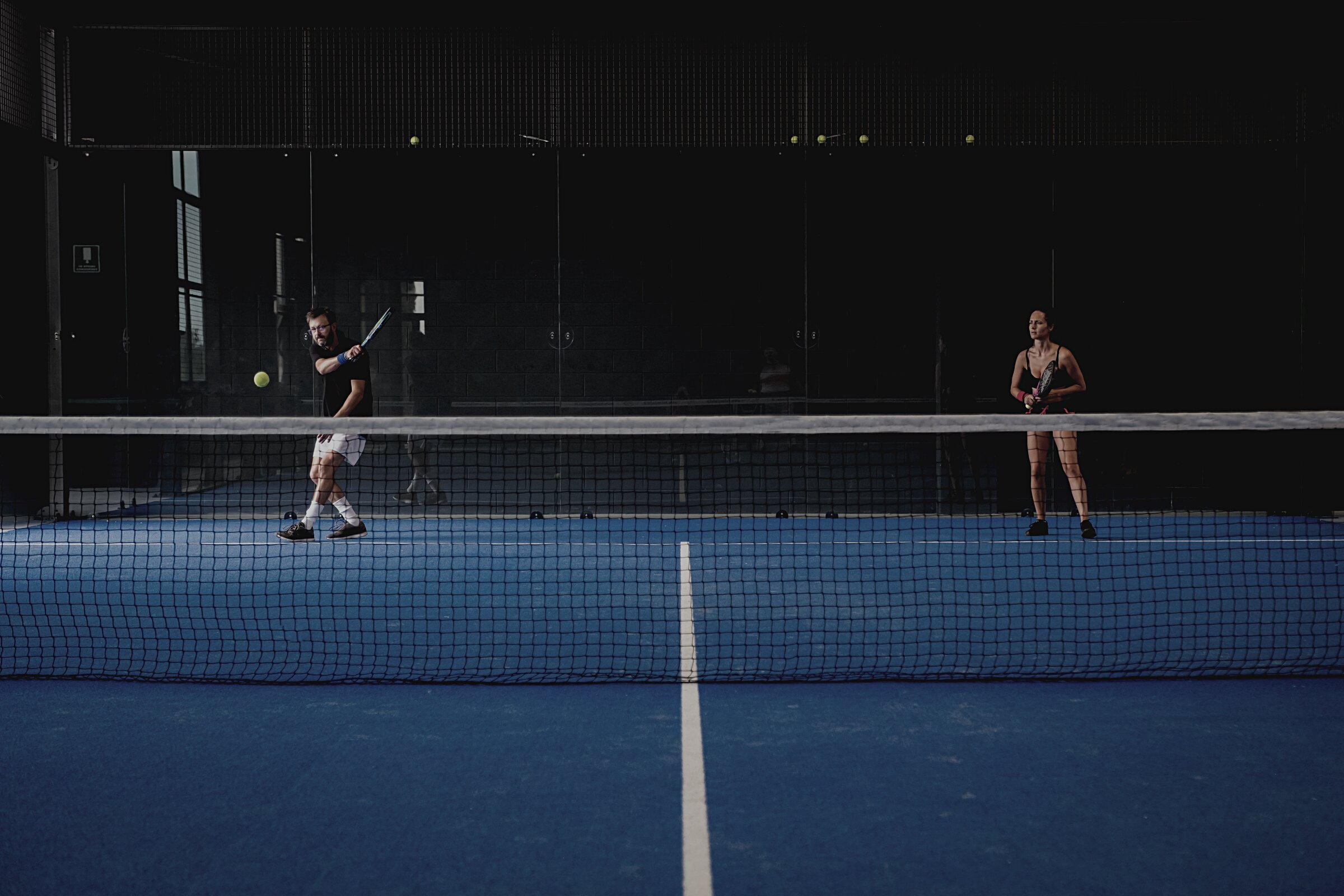 Mixed padel match in a blue grass padel court indoor behind the net